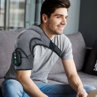 Smiling young man seated on grey sofa wearing heated compression shoulder brace with LED display