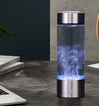 Hydrogen Water Bottle Generator glowing blue on dark desk beside open laptop