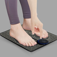 Person in grey leggings pressing control button on black EMS Foot Massage Mat