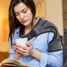 Load image into Gallery viewer, Woman holding cup reading while wearing grey heated compression shoulder brace at home
