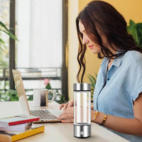 Woman at desk using laptop beside silver hydrogen water bottle generator