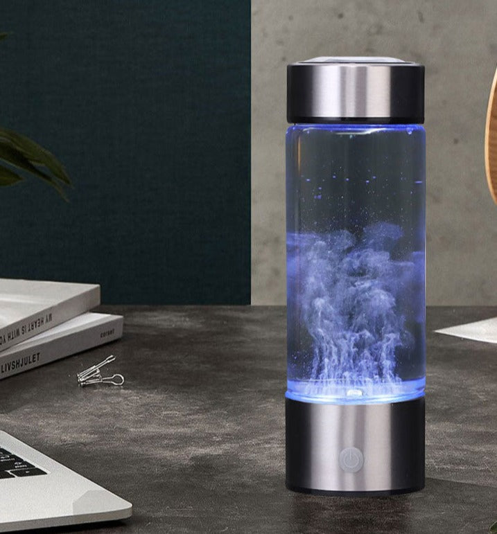 Hydrogen Water Bottle Generator glowing blue on dark desk beside open laptop