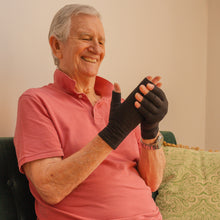 Load image into Gallery viewer, Smiling elderly man wearing black Therapeutic Heat Gloves indoors
