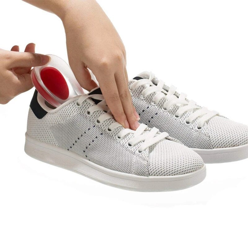 Hands inserting a red gel heel cup into the heel of a white mesh sneaker beside a matching pair of shoes