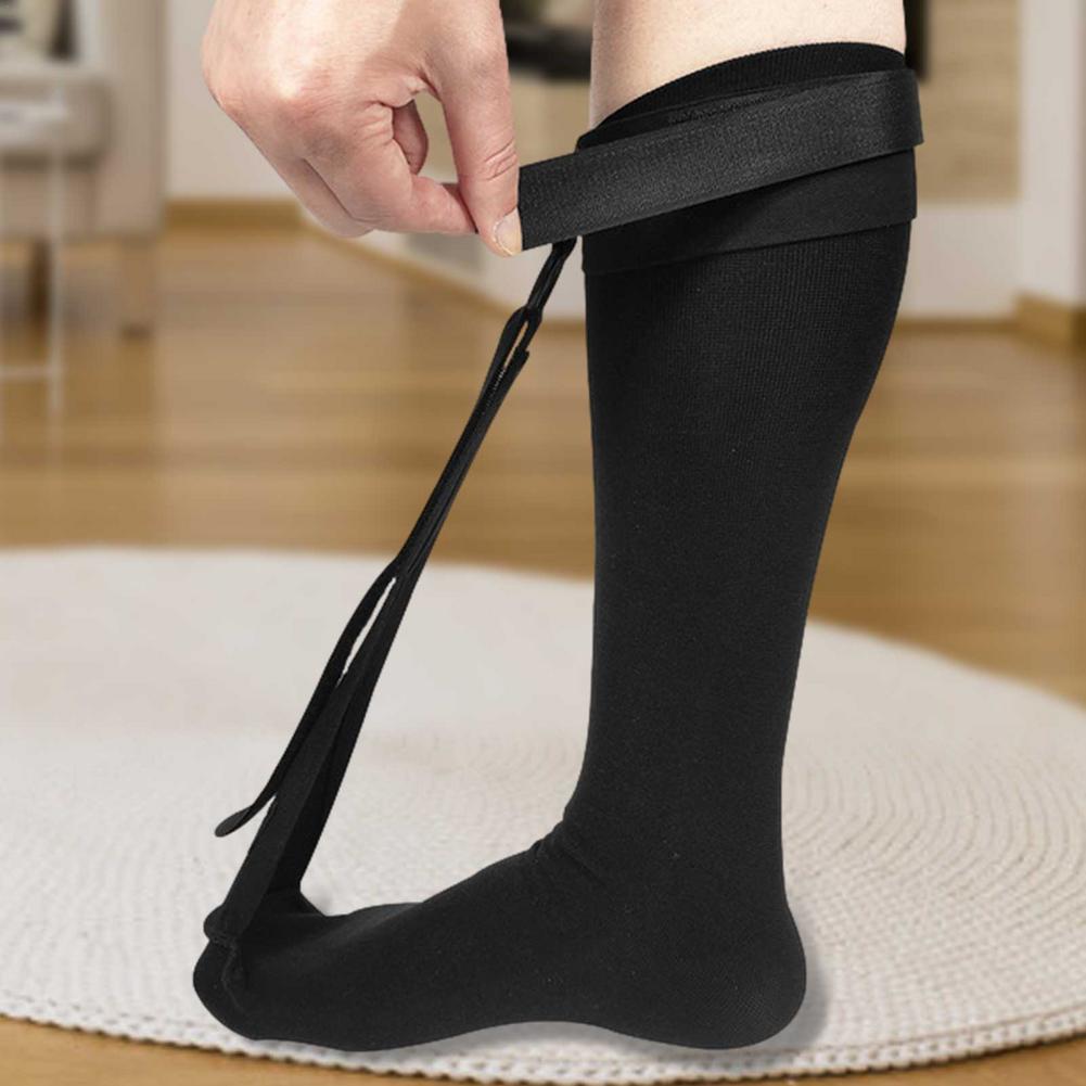 Person pulling the calf strap of a black plantar fasciitis night splint sock onto their lower leg at home