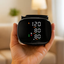 Load image into Gallery viewer, Hand holding a black wrist blood pressure monitor face-on, displaying SYS, DIA and PUL readings on LED screen
