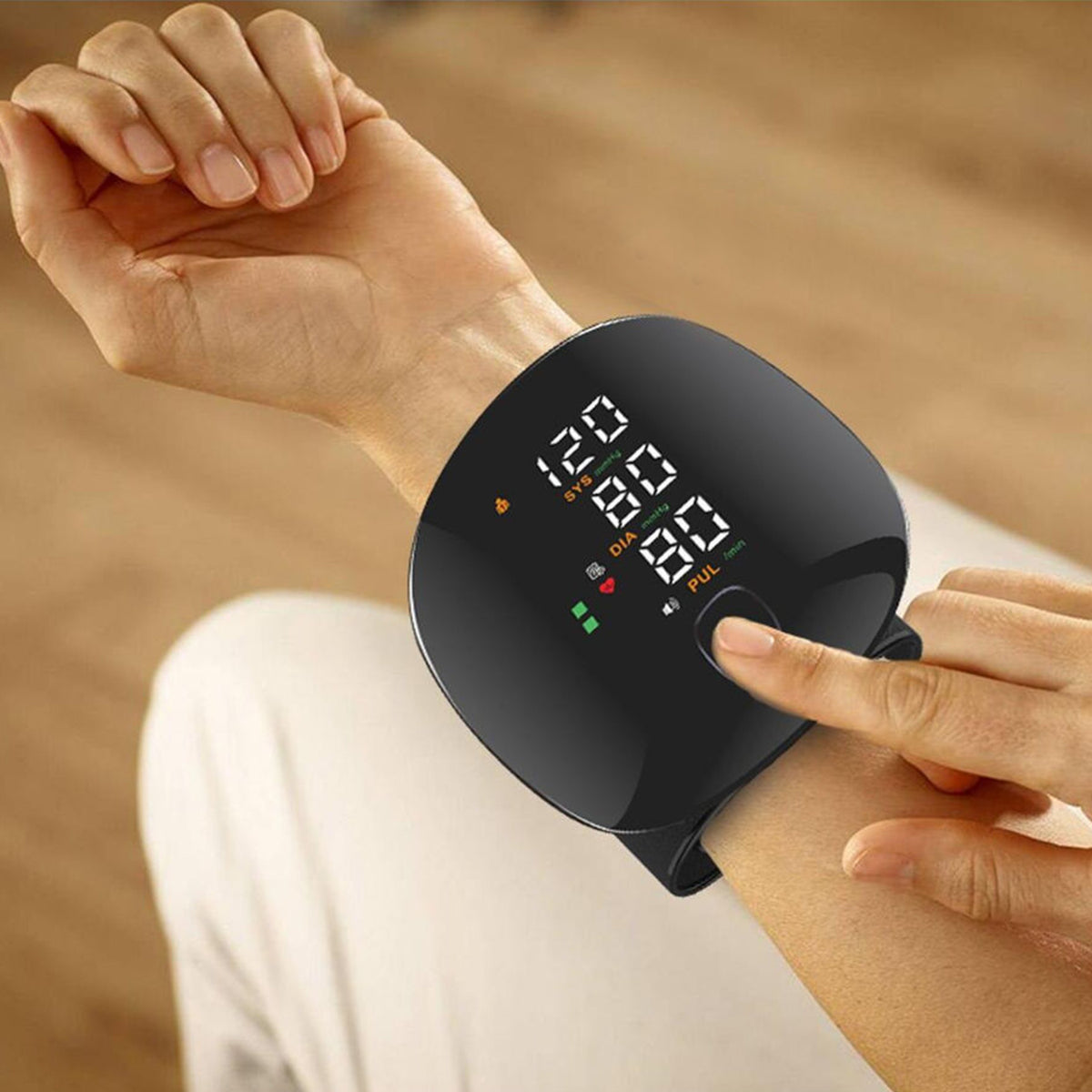Person pressing the start button on a black wrist blood pressure monitor displaying SYS, DIA and pulse readings