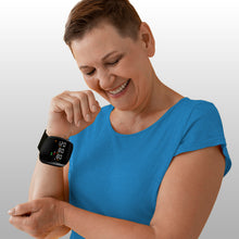 Load image into Gallery viewer, Smiling woman in blue top reading her wrist blood pressure monitor showing 120/80 mmHg result
