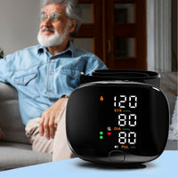 Black wrist blood pressure monitor on table showing 120/80 reading, smiling older man relaxing on sofa behind