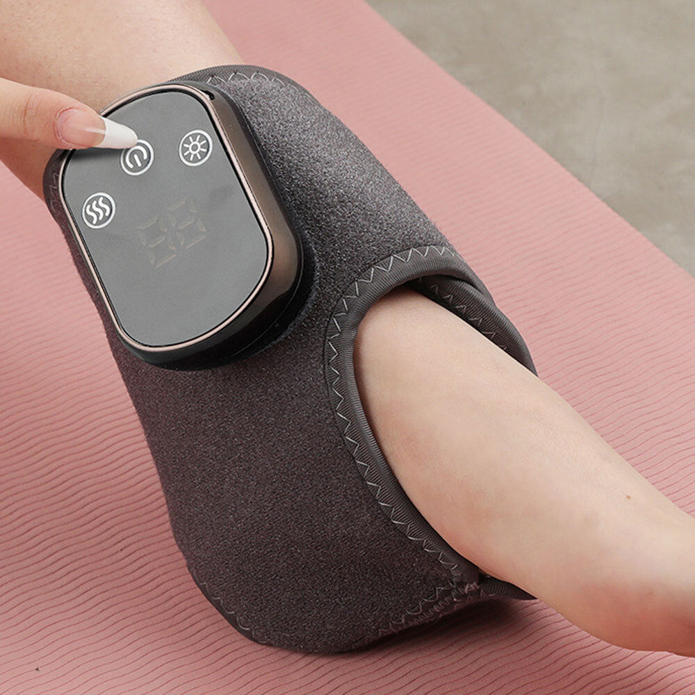 Woman pressing button on grey ankle massager wrap worn on ankle resting on a pink yoga mat