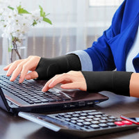 Person wearing black gel thumb support gloves typing on a laptop at an office desk