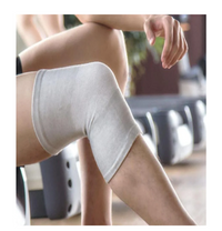 Person seated indoors wearing a grey bamboo knee support sleeve on a bent knee